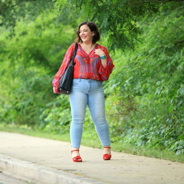 Alison Gary of Wardrobe Oxygen wearing a red printed chiffon blouse from Free People with light wash ankle jeans, carrying a black leather tote bag and wearing red suede platform heeled sandals