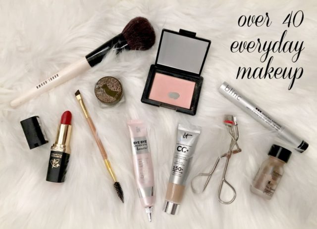 Photo of makeup laid out on. sheepskin rug. An opened compact of blush, tube of lipstick, tubes of concealer and CC cream and mascara. An eyelash curler, a few brushes, a pot of eyebrow color and jar of eyelid concealer.