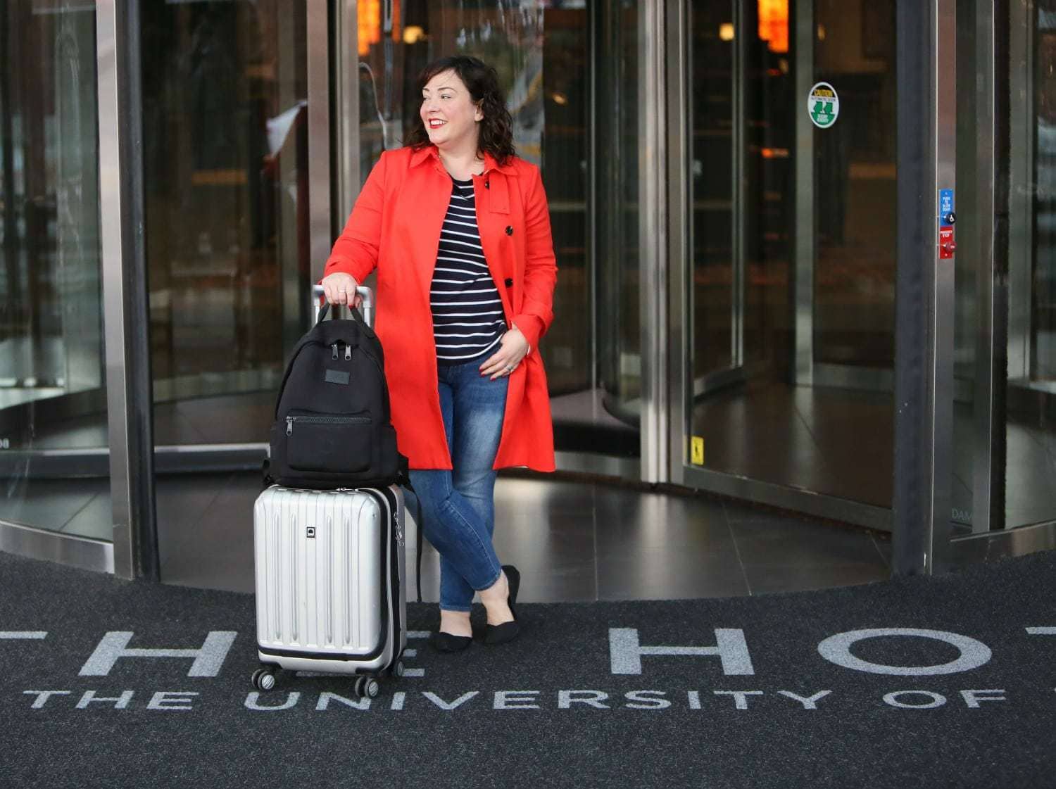 Wardrobe Oxygen in a red orange trench from Banana Republic with Talbots striped top, Banana Republic ankle jeans, Rothy's flats, Dagne Dover backpack and Delsey spinner suitcase