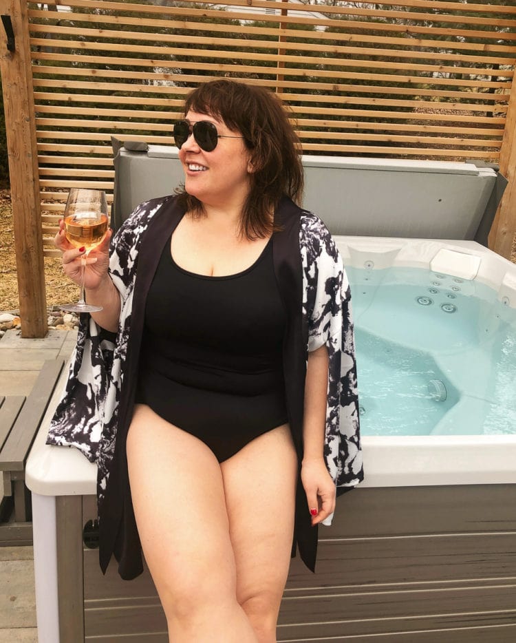 woman in a black lands end tugless tank swimsuit and a kimono swim coverup sitting next to a hot tub with a glass of wine in her hand