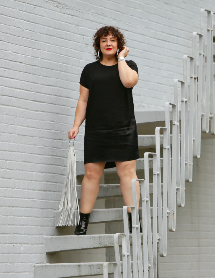 Wardrobe Oxygen in a black crepe dress from Universal Standard with a white fringe bag from KARA and black patent leather wide width ankle booties from ASOS