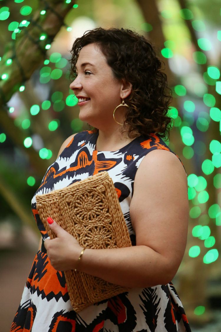 Alison holding a raffia woven foldover clutch and wearing portrait hoop earrings from woman-owned jewlery brand REALM