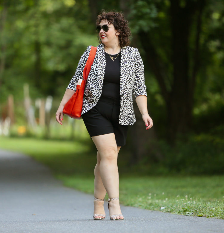 Alison wearing a leopard print blazer with a black tee and black shorts carrying an orange Clare V tote