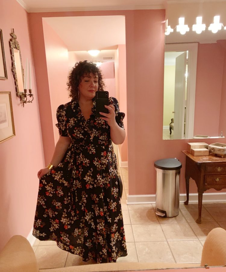 Alison Gary of Wardrobe Oxygen in a navy floral wrap midi dress taking a mirror selfie in a pink room