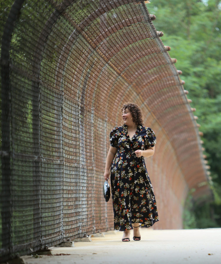 woman in a navy floral midi wrap dress walking along a city overpass looking to the side