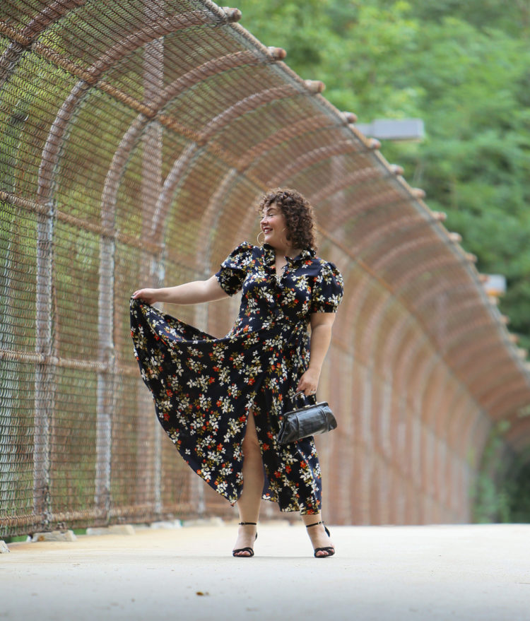 Woman in a navy floral midi dress holding up the edge of the dress to show the volume, smiling and looking away