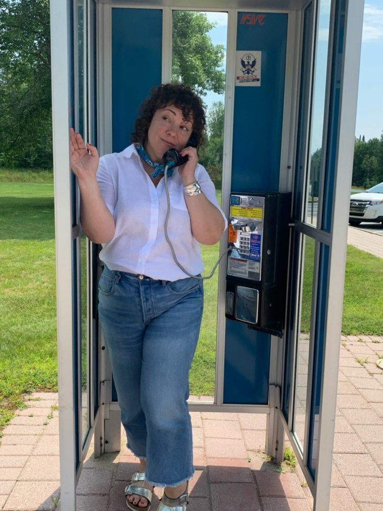 woman in white linen shirt and cropped jeans standing in a phone booth