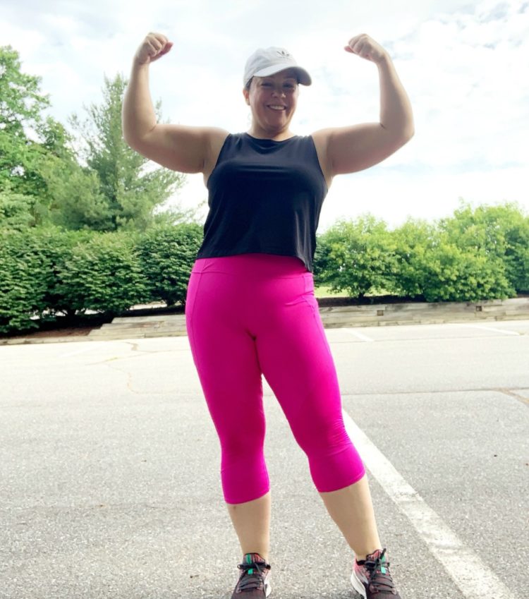 woman in black crop top and magenta leggings flexing her muscles