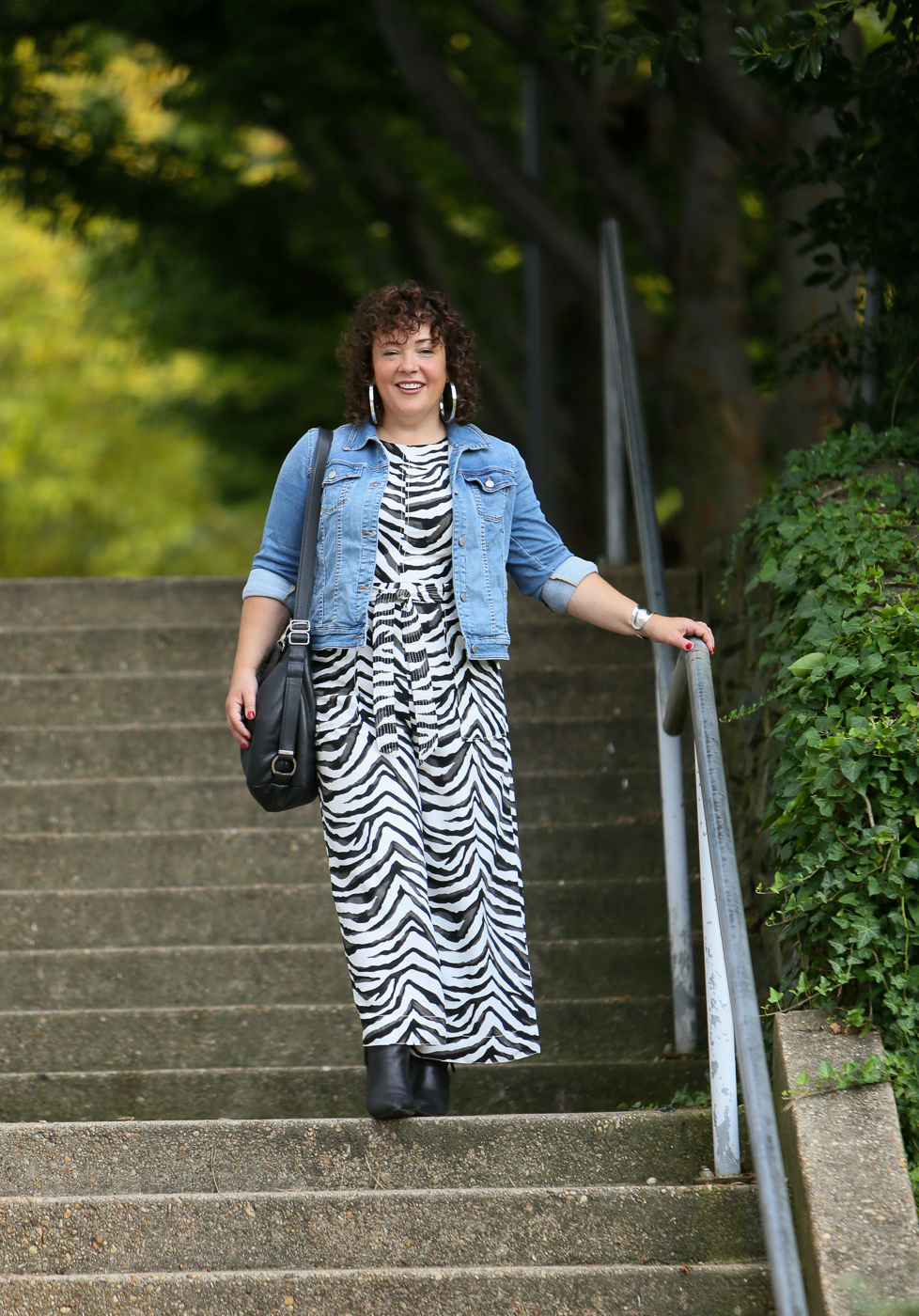 Styling a summer jumpsuit for fall - tips on how to do this successfully by Wardrobe Oxygen who is wearing a zebra print Banana Republic jumpsuit with a denim jacket and black ankle booties by Clark's and carrying a Rough & Tumble handbag in black leather.