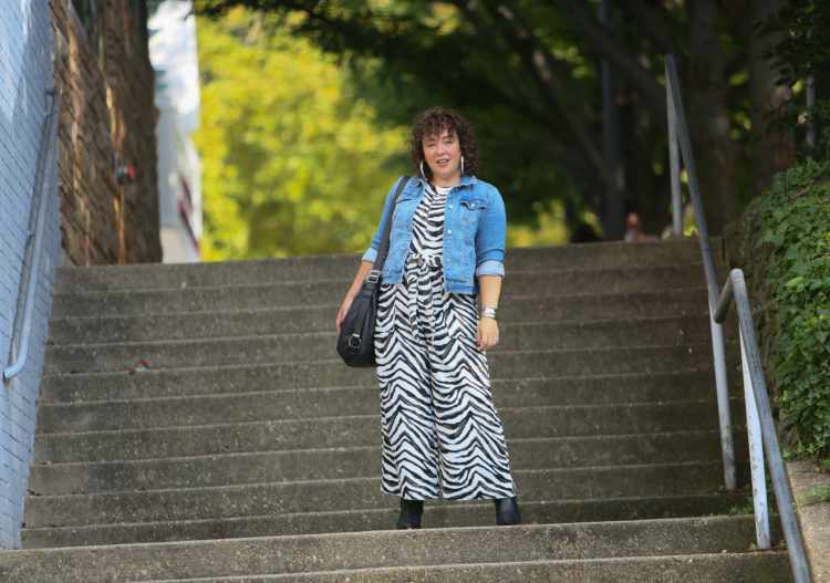 Styling a summer jumpsuit for fall - tips on how to do this successfully by Wardrobe Oxygen who is wearing a zebra print Banana Republic jumpsuit with a denim jacket and black ankle booties by Clark's and carrying a Rough & Tumble handbag in black leather.