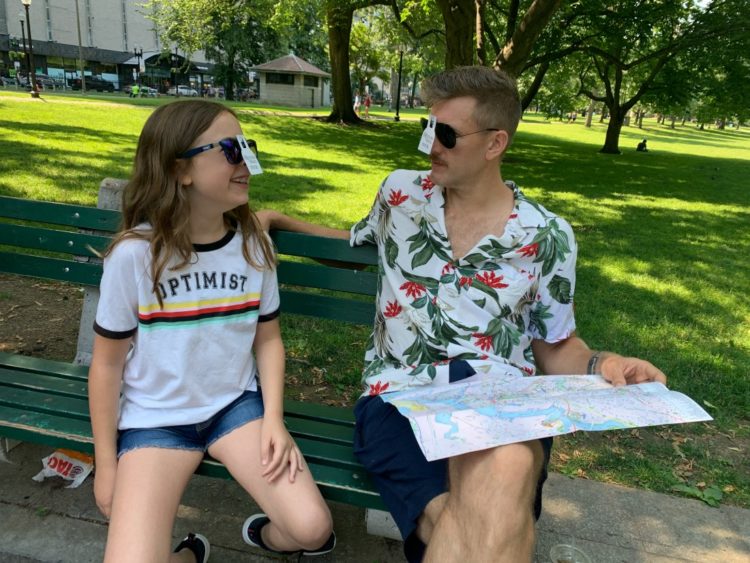 Emerson and Karl wearing sunglasses with their Freedom Trail pins stuck to them looking at each other and smiling