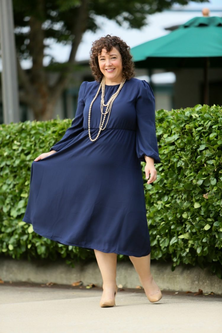 woman in a navy dress with two long strands of pearls and nude colored heels