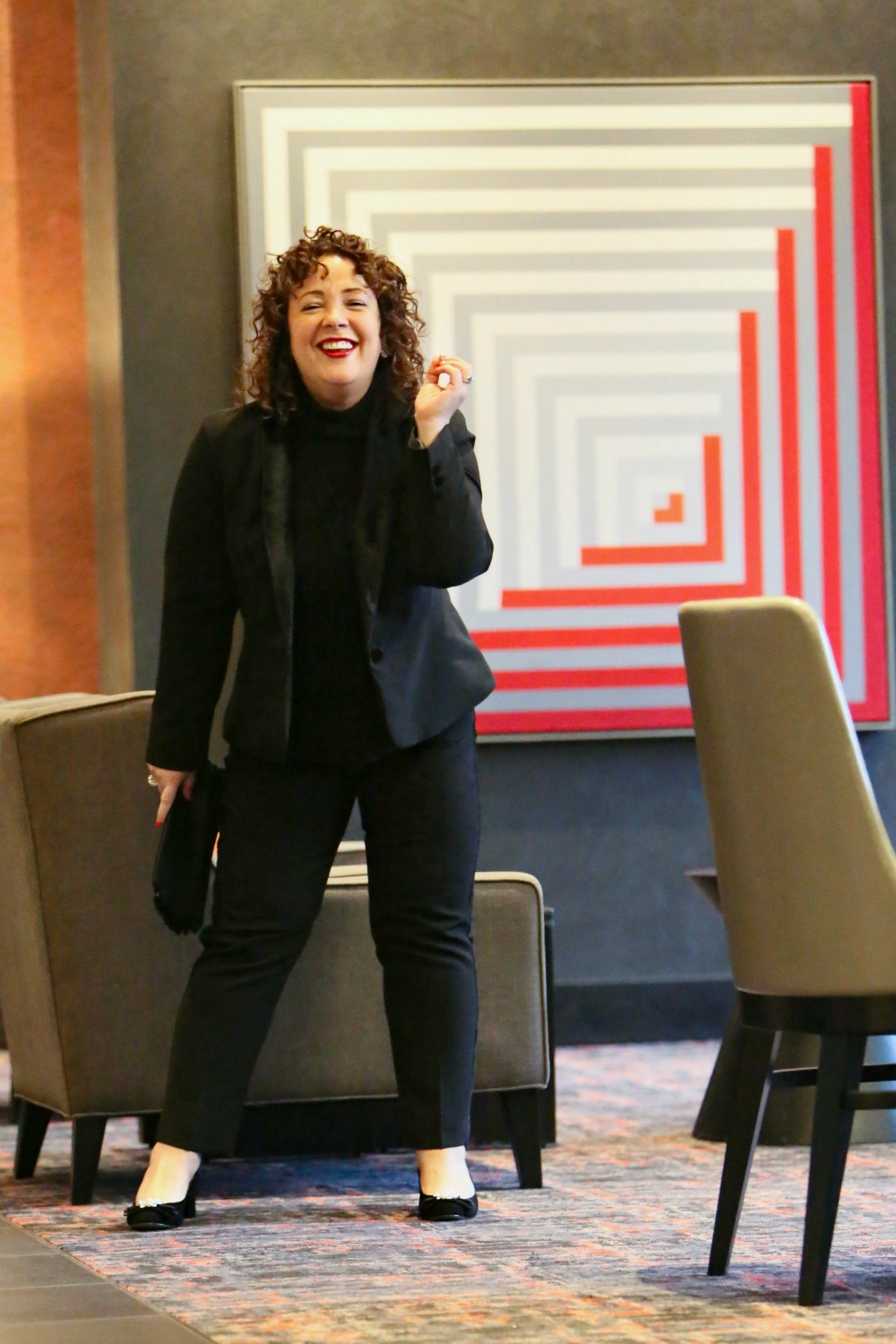 Woman in a black pantsuit with black cashmere and a black suede clutch in her hand