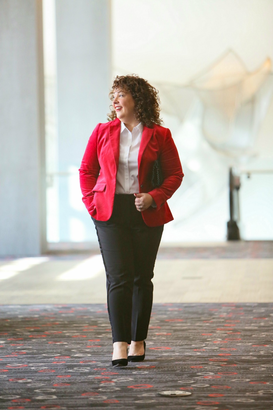 Alison in a red velvet blazer looking out the window of a hotel lobby