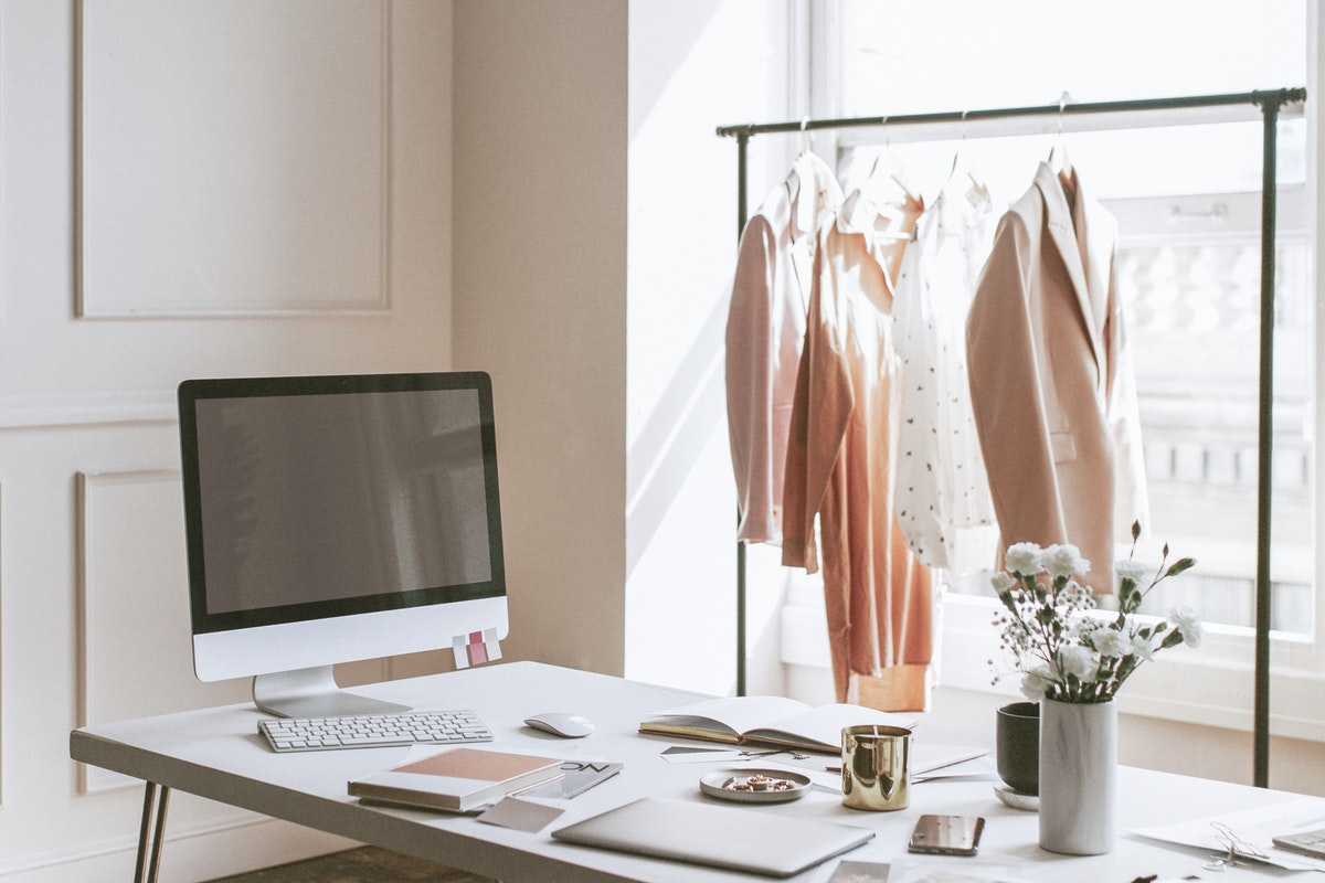 clothing on a rack behind a desk with a computer