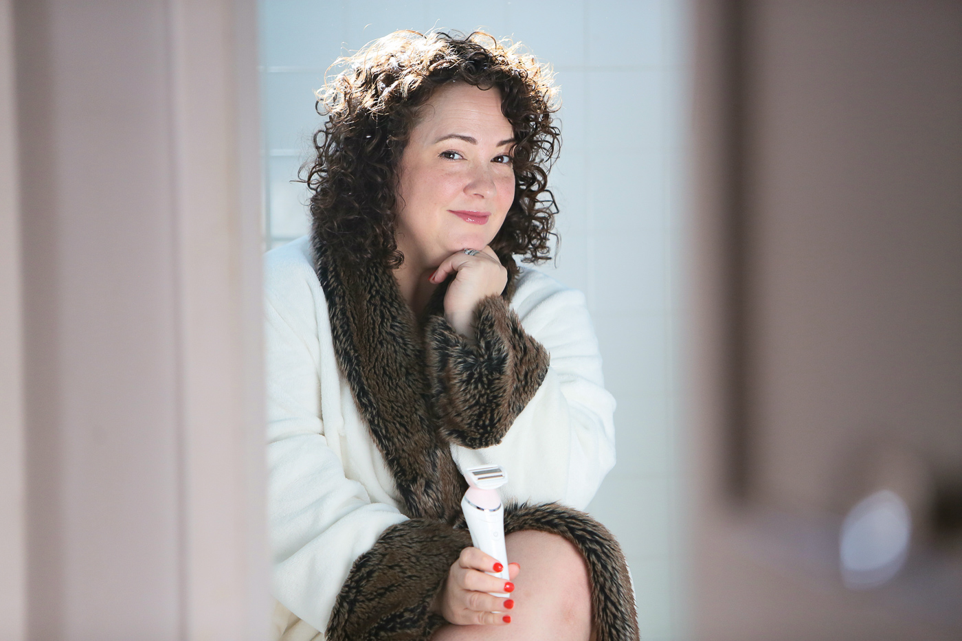 woman in bathrobe smiling at the camera while holding an electric razor