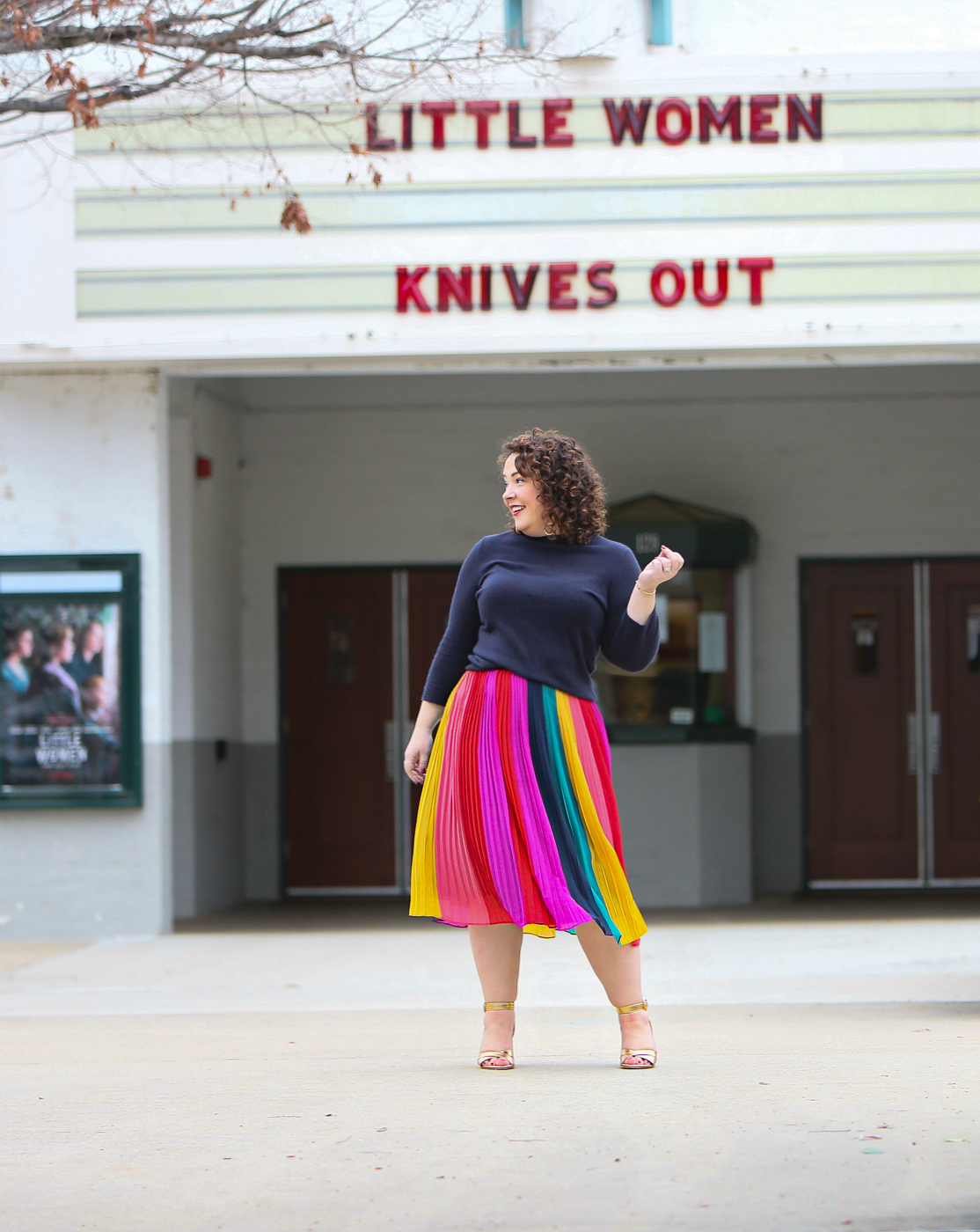 woman in a rainbow striped skirt and navy sweater standing in front of a movie theater