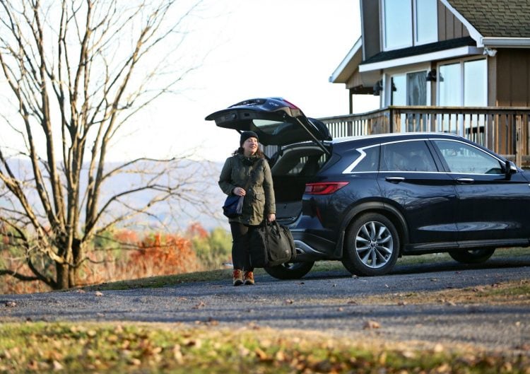 A petite over-women unpacking a car at a cabin in the mountains, pulling out the Tom Bihn Aeronaut 45 bag, holding it with the hand straps.