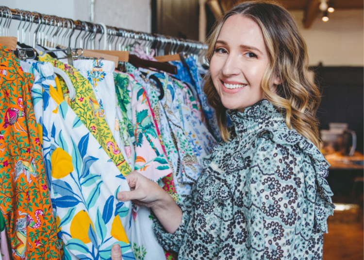 Image of Amy Voloshin in a blue and white printed top standing next to a rolling rack full of Printfresh sleepwear