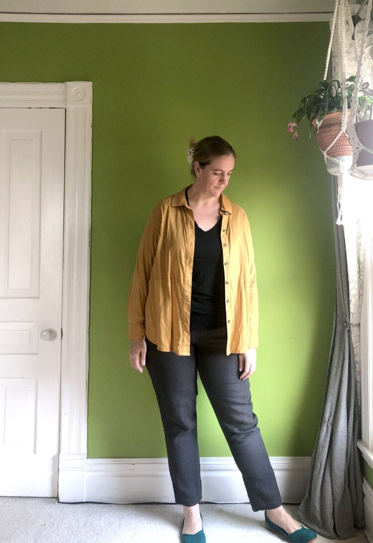 Woman in black ankle pants and black t-shirt topped with a goldenrod button front long sleeve shirt open and worn like a jacket.