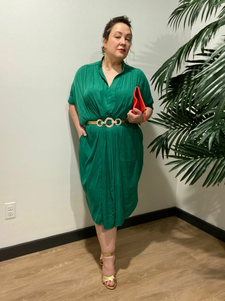 Alison Gary of Wardrobe Oxygen in an emerald green ever by X dress styled with a sparkly stretch belt, gold heeled sandals, and a tomato red foldover leather clutch.