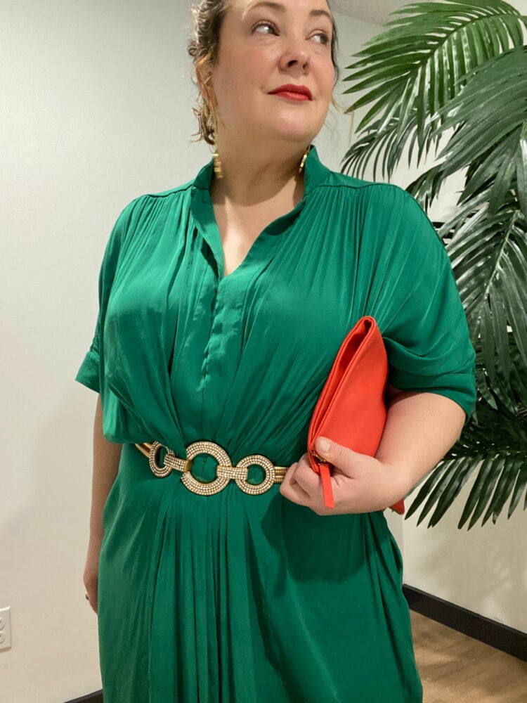 Alison Gary of Wardrobe Oxygen in an emerald green ever by X dress styled with a sparkly stretch belt, gold heeled sandals, and a tomato red foldover leather clutch.