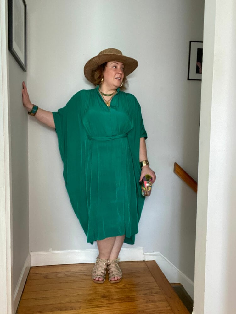 Alison wearing the green ever by X dress styled like a caftan with a straw hat and gladiator sandals