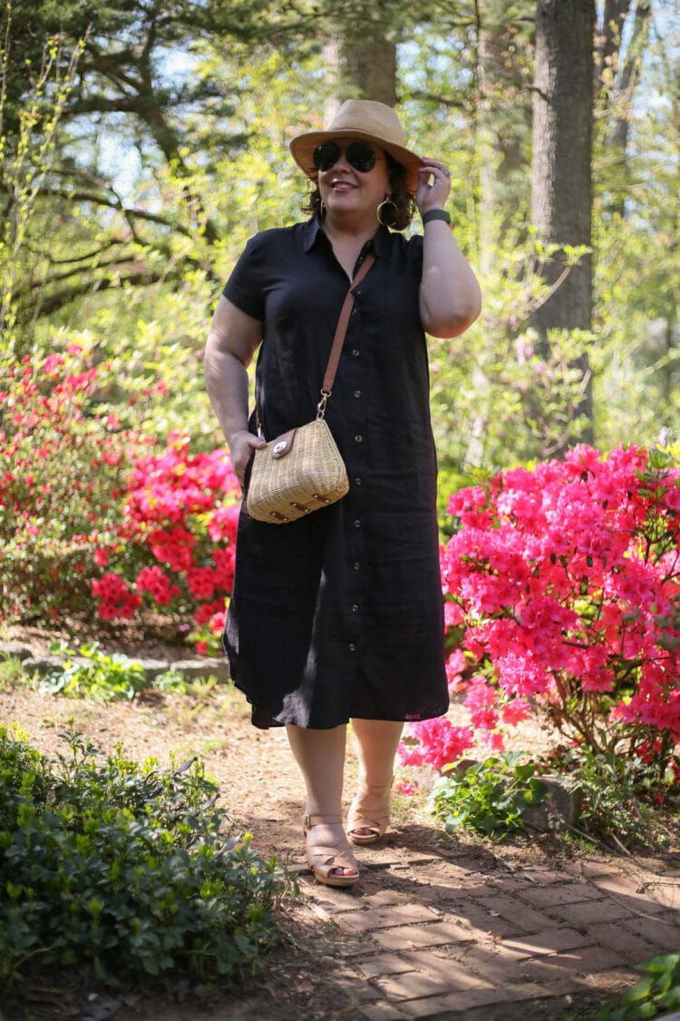 Alison wearing the Dune linen shirtdress in black with a straw hat, wicker bag, and clog sandals