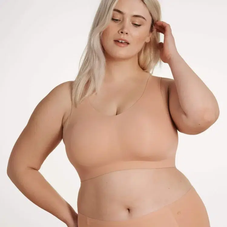 A blonde curvy model wearing the Evelyn & Bobbie Defy bra in beige 