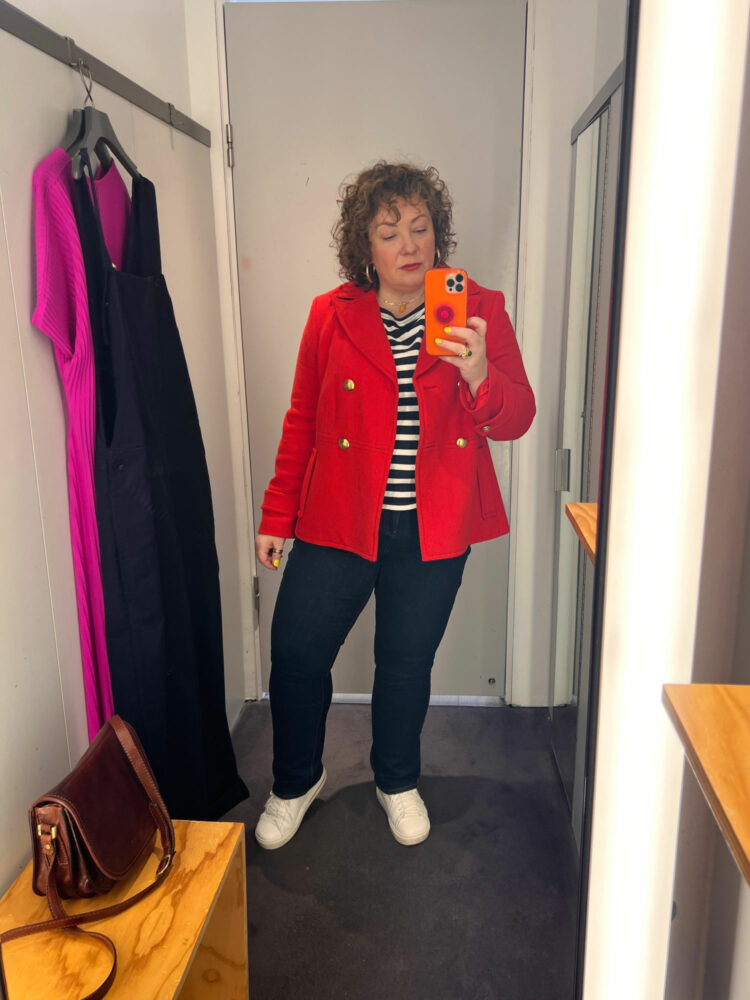 woman in a store's fitting room wearing a red wool peacoat and a pair of jeans