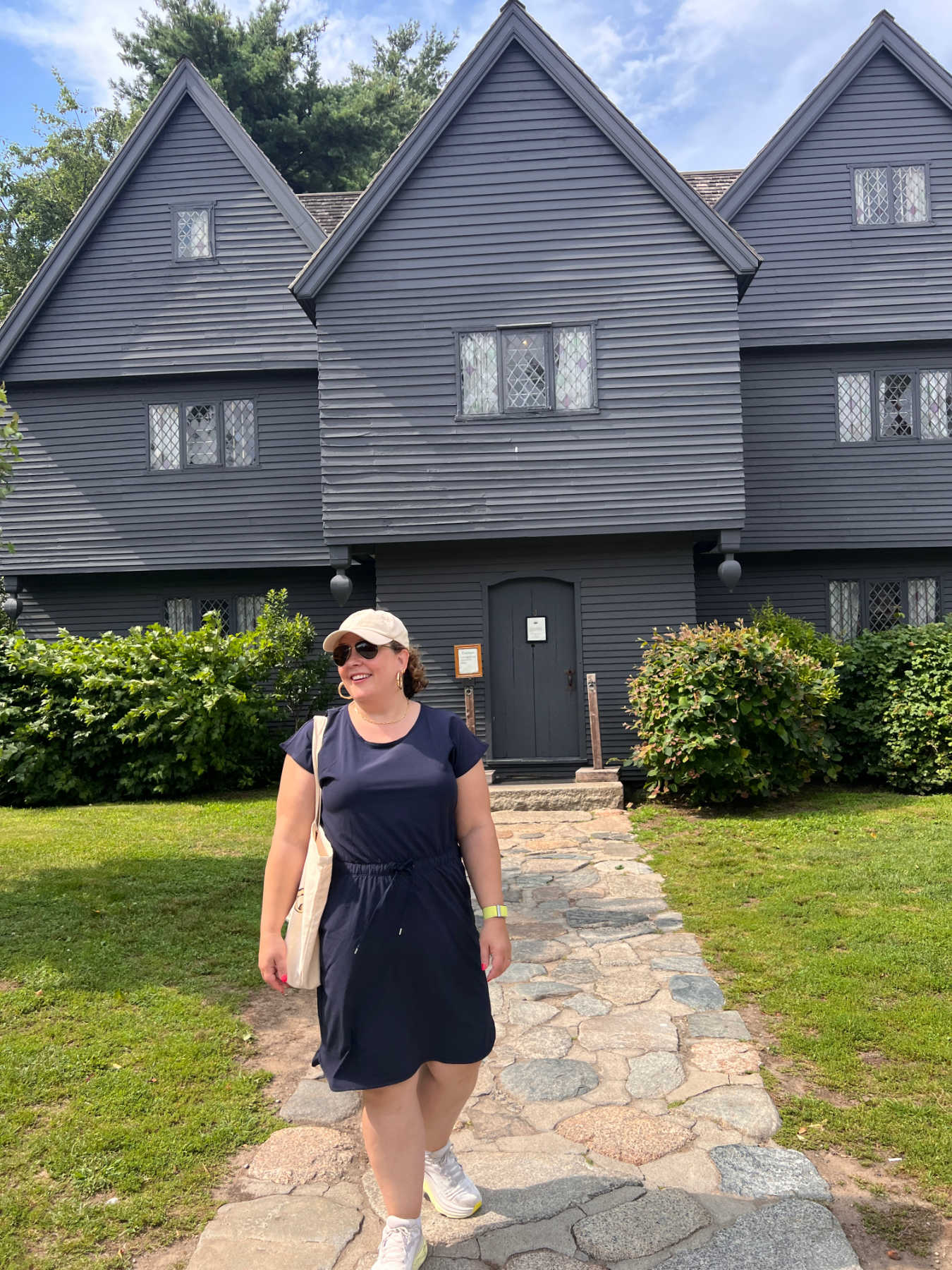 woman in a navy Talbots active dress and sneakers in front of the Salem Witch House in Salem, MA