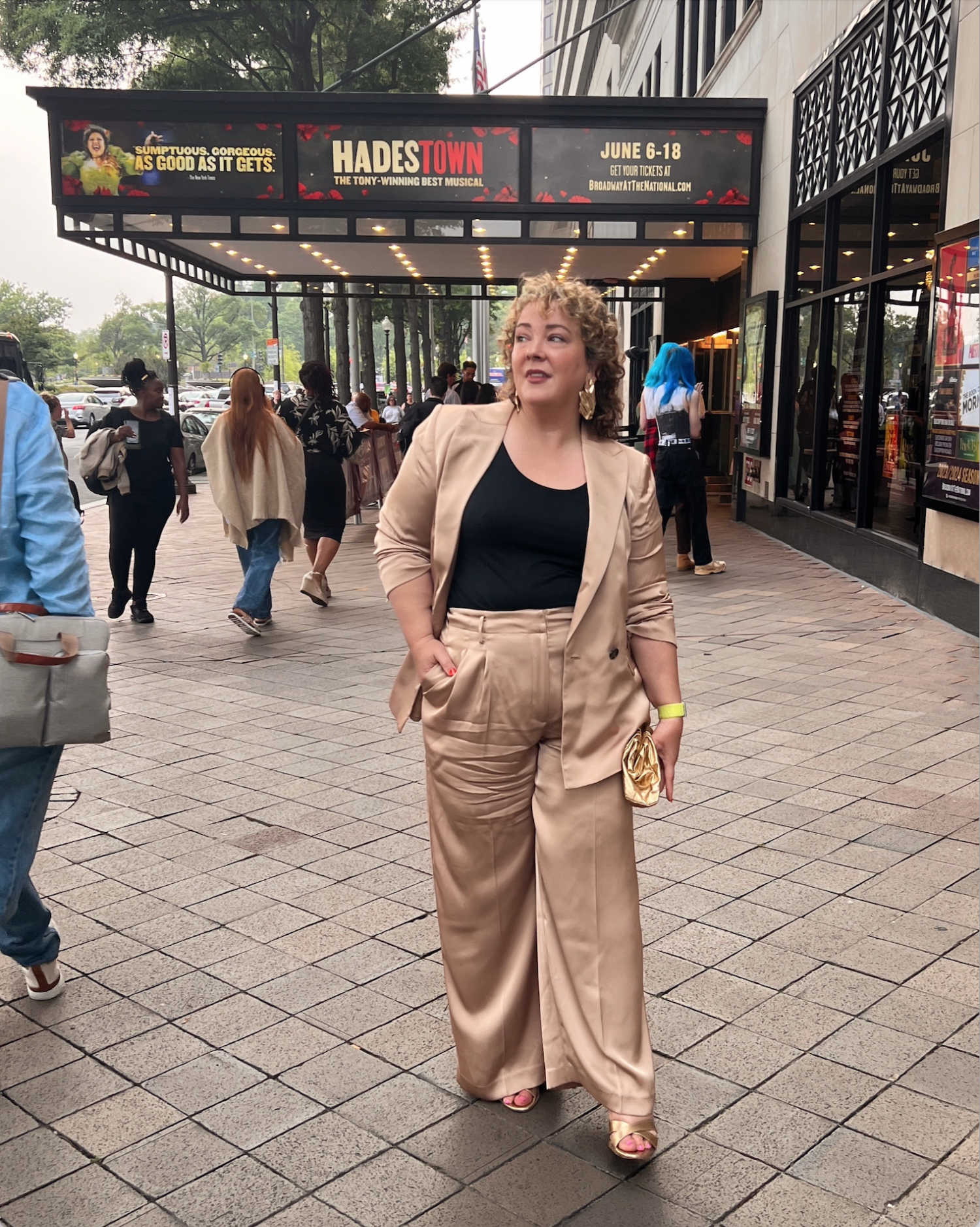 Alison Gary of Wardrobe Oxygen in front of National Theatre in Washington DC. She is wearing a tan satin pantsuit with a black shell underneath and gold heels