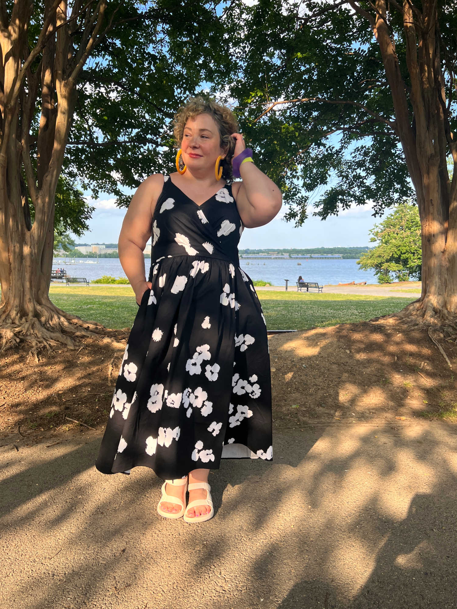 woman in a black and white floral poplin sundress in front of a riverfront.