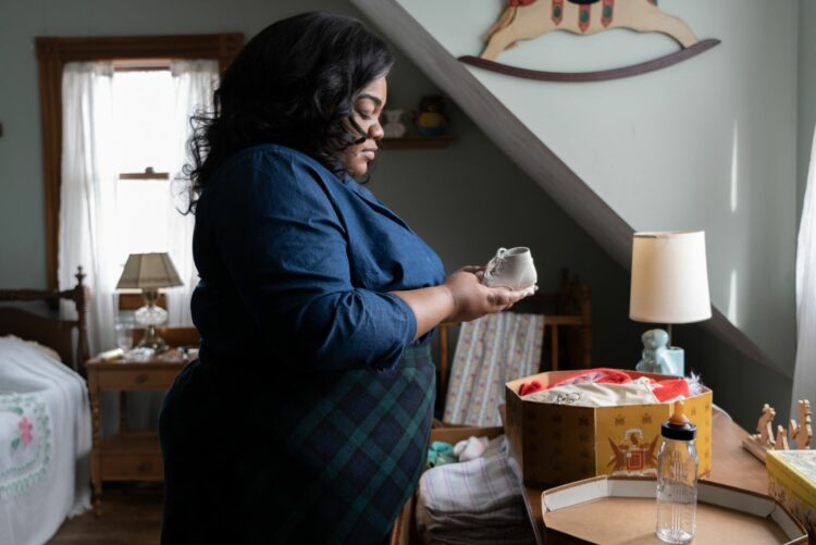 Scene from the movie The Holdovers showing actress Da'Vine Joy Randolph in a bedroom, holding a baby shoe in her hands, looking down at the shoe with a sad look on her face