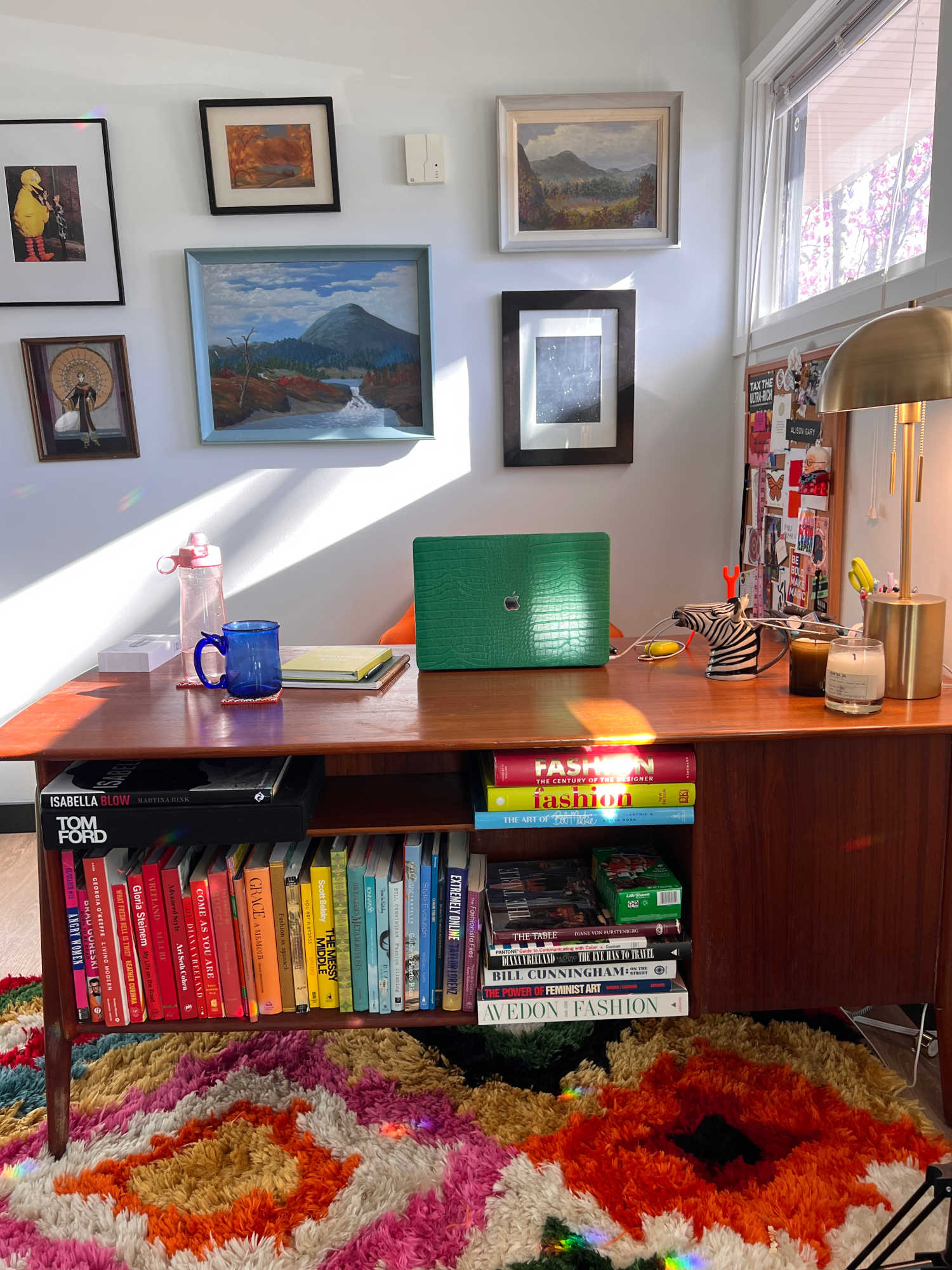 A view of the front of an MCM dsk full of colorful books, in front of a gallery wall