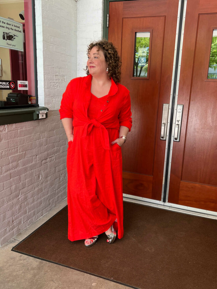 Alison wearing the Universal Standard promenade linen jumpsuit in orange with the Dune linen tunic tied over it.