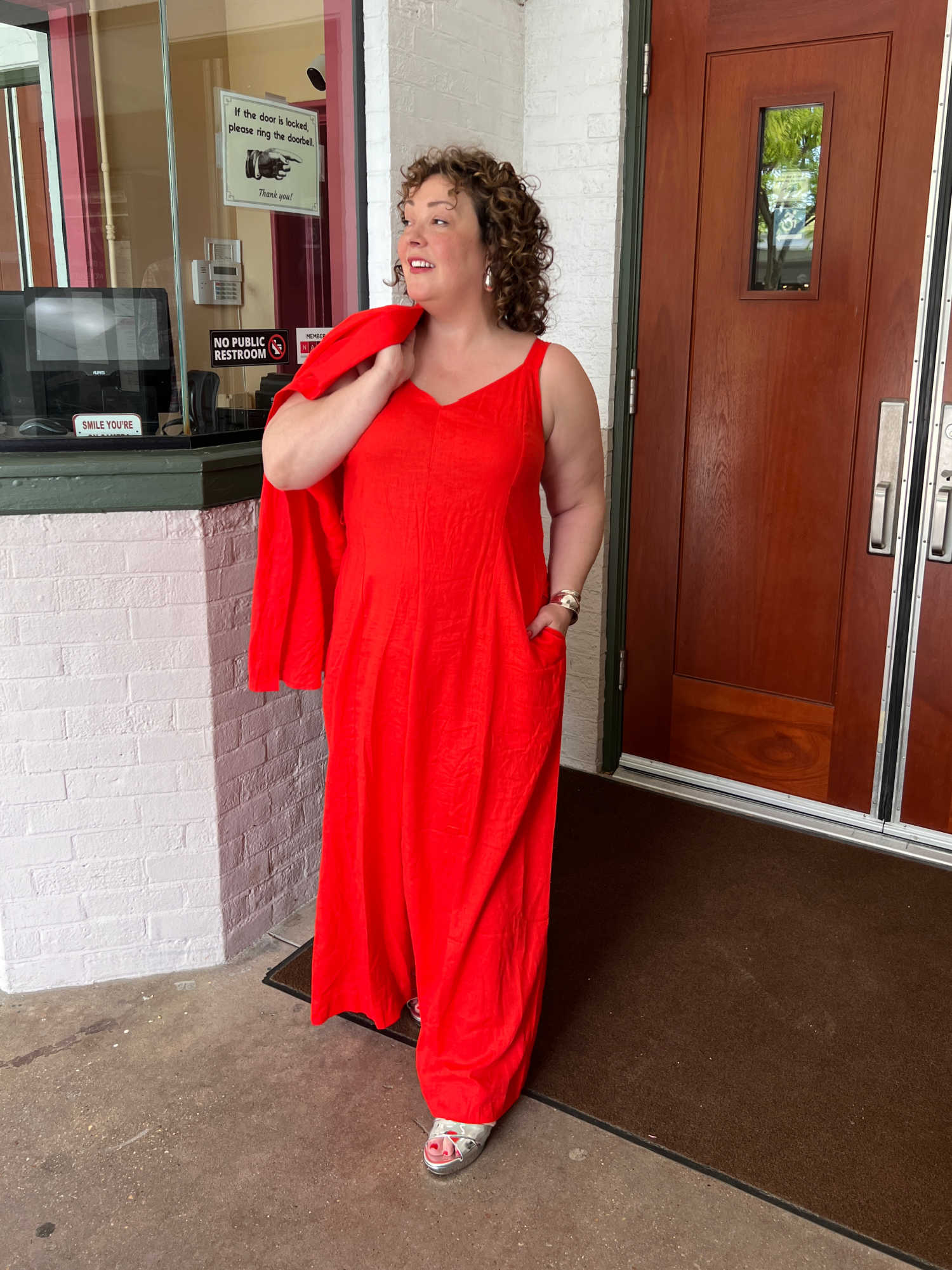 Alison in an orange linen adjustable strap jumpsuit with a matching shirt over her shoulder