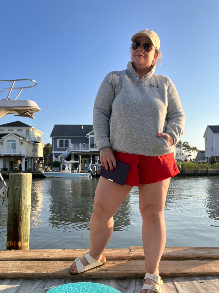 Alison in a tan canvas ball cap, gray L.L. Bean sweater fleece, and red UNiversal Standard sunny shorts