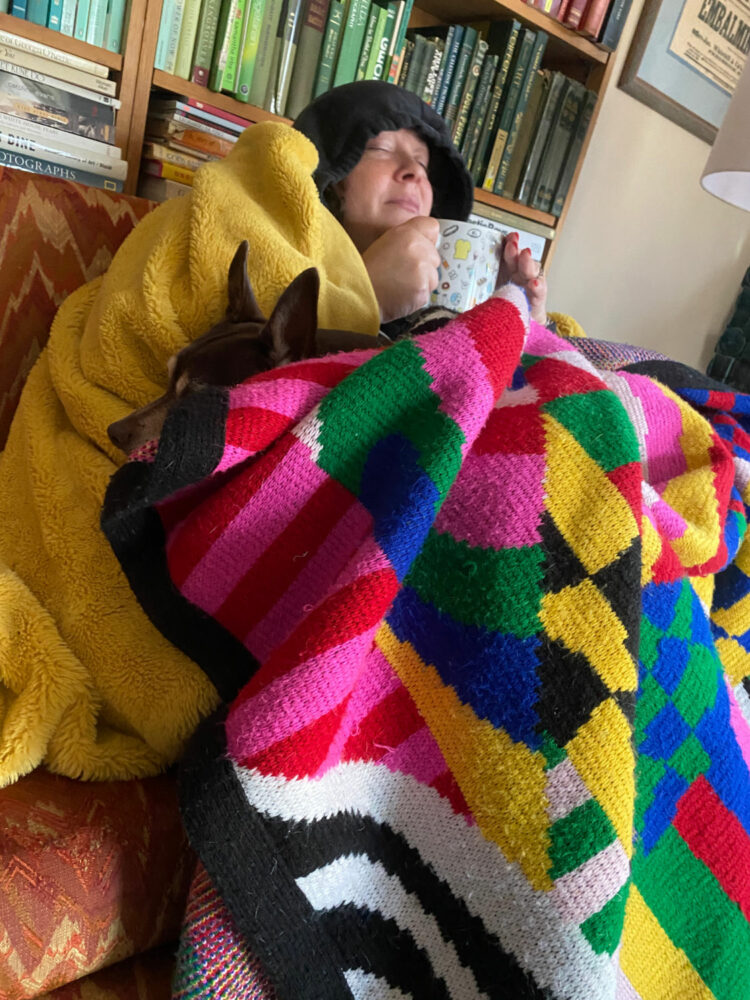 alison gary of wardrobe oxygen with her dog curled up under blankets on her sofa