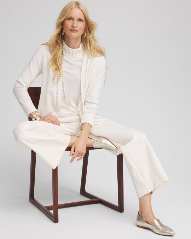 Woman with blonde hair sitting in a chair wearing winter white sweater and matching wide leg pants and champagne metallic loafers