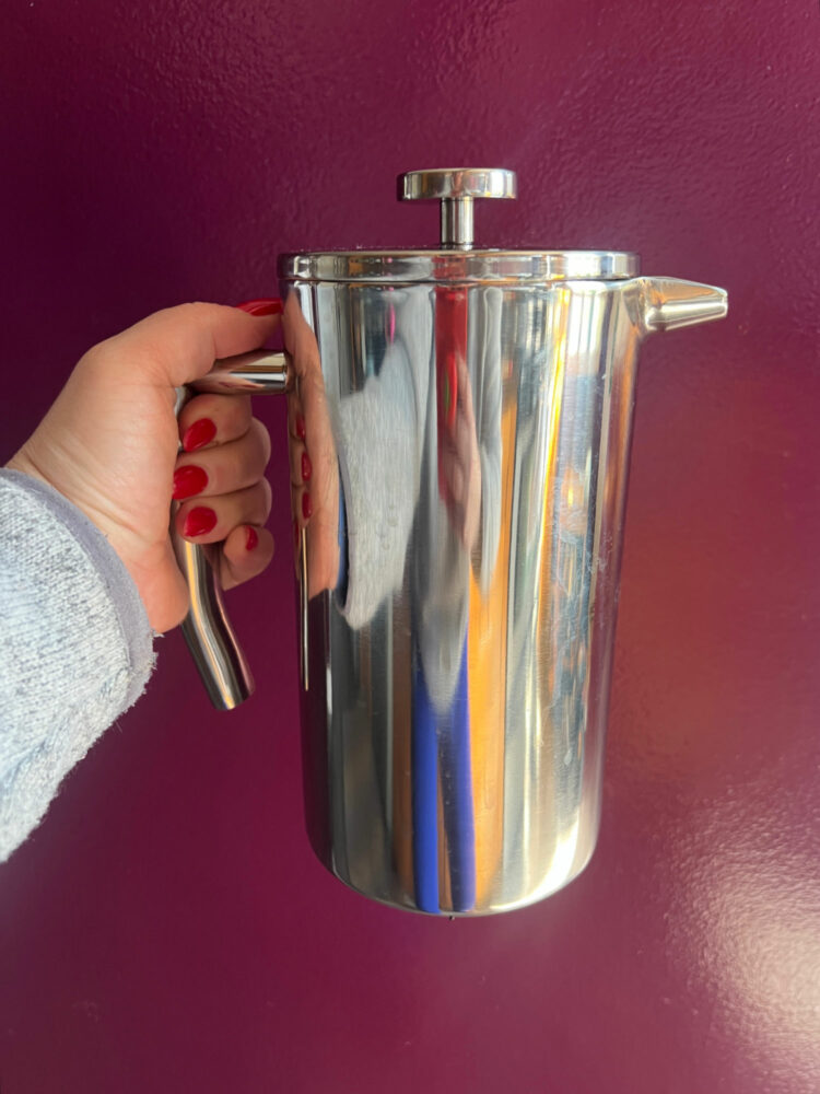 woman's hand holding a stainless steel French press from Quince