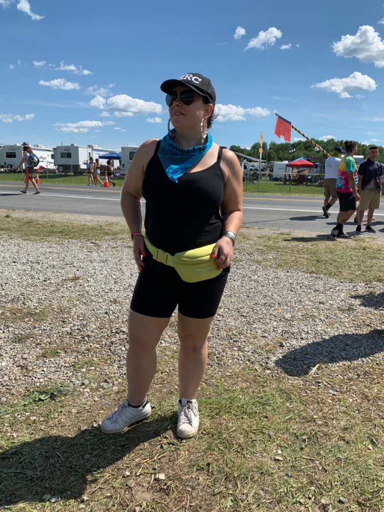 black tank and bike shorts woman in a black tank and bike shorts and a neon belt bag at a music festival. She is over 40 and wearing a baseball cap.