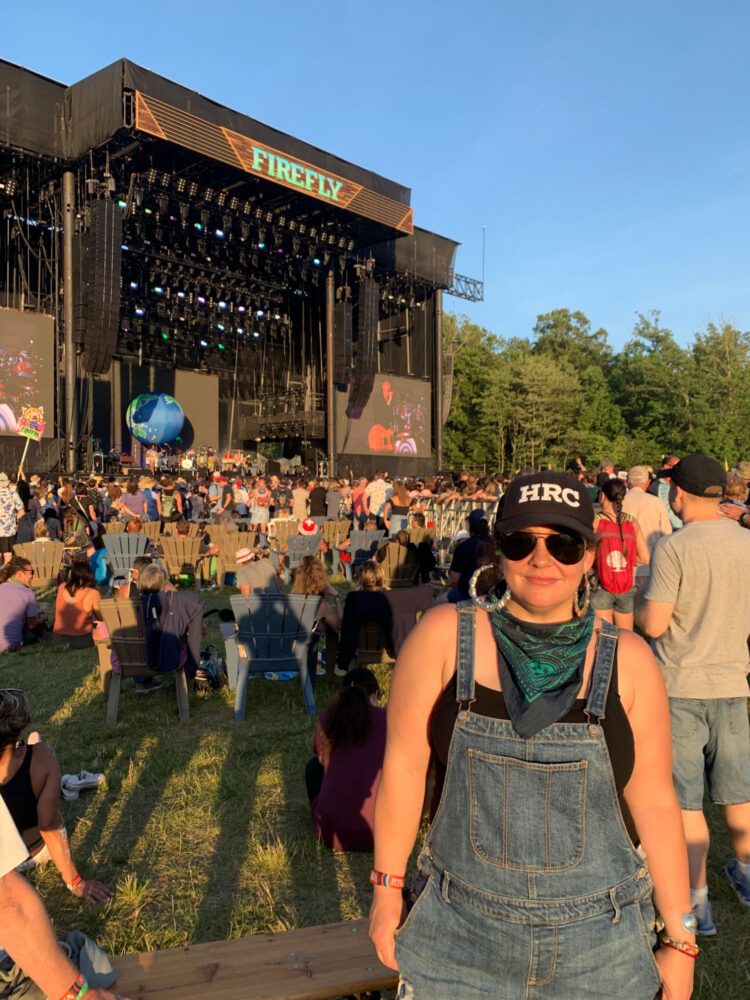 shortalls and a baseball cap Woman in shortalls and a baseball cap in front of a stage where Vampire Weekend is performing at the 2019 Firefly music festival
